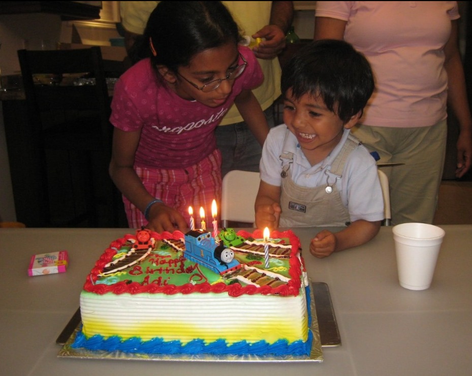 me as a kid, smiling next to a Thomas the Tank Engine birthday cake